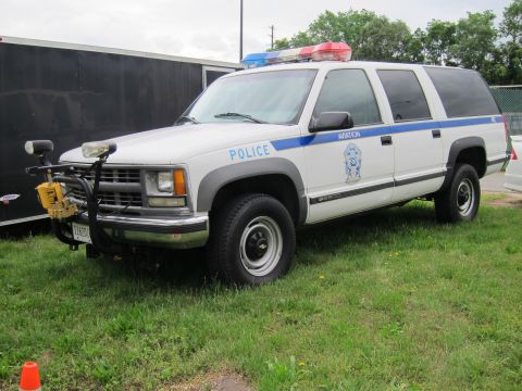 1991 Ford LTD Crown Victoria - white and gray Chevrolet Suburban police SUV marked Aviation with a winch and brush guard on grass.