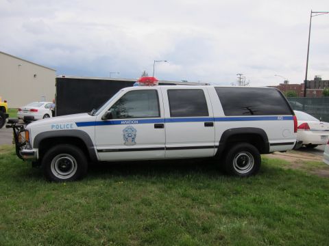 1991 Ford LTD Crown Victoria - white and gray Chevrolet Suburban police SUV marked Aviation with blue stripe parked on grass.