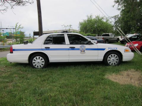 1991 Ford LTD Crown Victoria - white Ford Crown Victoria police sedan with a blue stripe and roof light bar parked on grass.