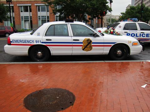 1991 Ford LTD Crown Victoria - white Ford Crown Victoria police sedan marked Emergency 911 parked on a wet brick city street.