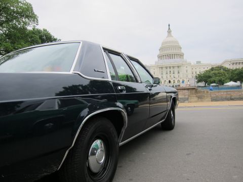 1991 Ford LTD Crown Victoria - dark green four-door sedan sits along a street with the U.S. Capitol dome rising in the cloudy background.