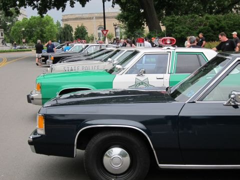 1991 Ford LTD Crown Victoria - lineup of vintage police cars, including a green-and-white State Police sedan, parked nose-to-tail at an outdoor show.