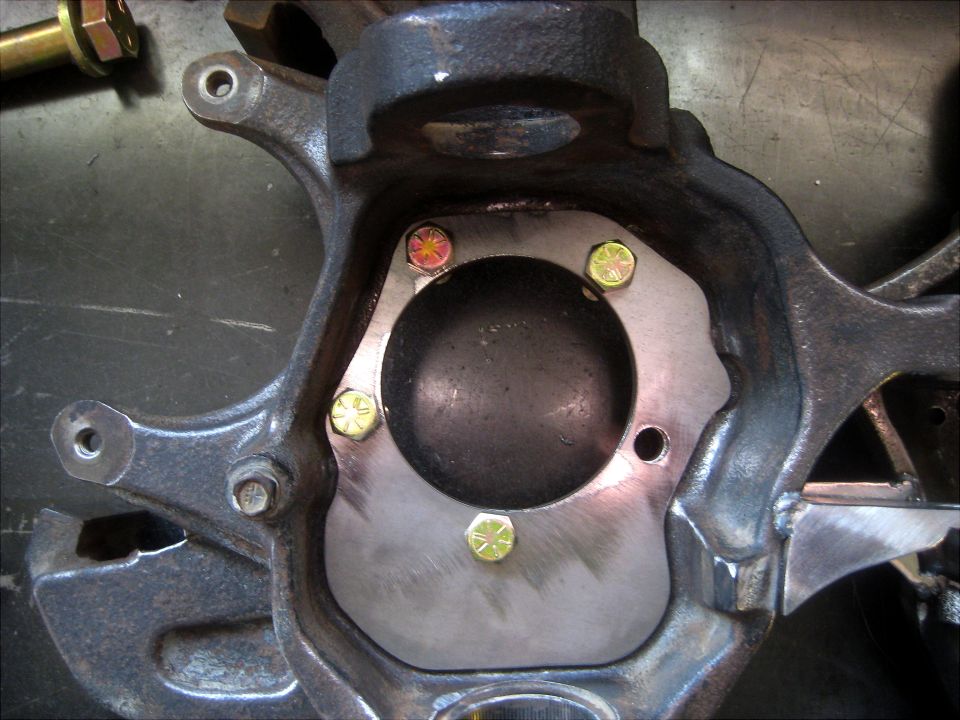 Steering knuckle with metal plate and bolts, viewed from front
