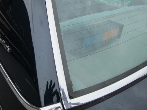 1991 Ford LTD Crown Victoria - Close-up of a dark car's rear quarter window, chrome trim and pillar, with a box visible on the rear deck inside.