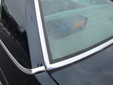 1991 Ford LTD Crown Victoria - Detailed close-up of a dark car's rear glass and chrome window surround with reflections on the glossy paint.