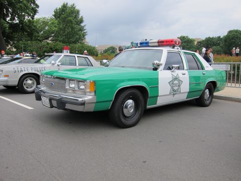 1991 Ford LTD Crown Victoria - green-and-white Sheriff patrol sedan with a Ford grille and roof lightbar parked at an outdoor car gathering.