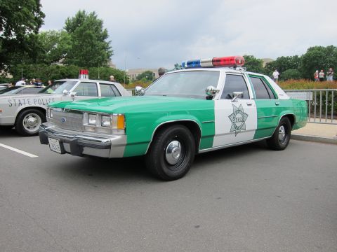 1991 Ford LTD Crown Victoria - Front three-quarter view of a green-and-white Sheriff patrol sedan with a Ford emblem, lightbar and star badge on the door.
