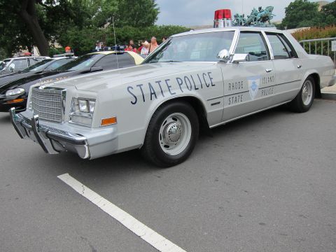 1991 Ford LTD Crown Victoria - silver Rhode Island State Police sedan with a chrome push bar and roof light parked among other vintage cars.