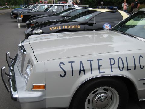 1991 Ford LTD Crown Victoria - silver State Police sedan front-and-center beside a black State Trooper car in a row of vintage patrol vehicles.