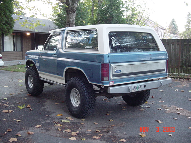 Blue and white lifted 1980s Ford Bronco rear quarter in driveway, Ford tailgate, fall leaves, 2003 date