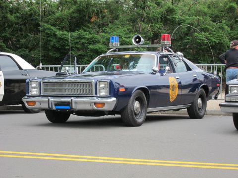 1991 Ford LTD Crown Victoria - dark blue vintage police cruiser with a roof light bar, spotlight and gold star door emblem parked on a city street.