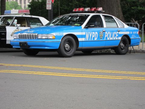 1991 Ford LTD Crown Victoria - light blue NYPD police sedan with white striping and a red roof light bar parked on a city street.