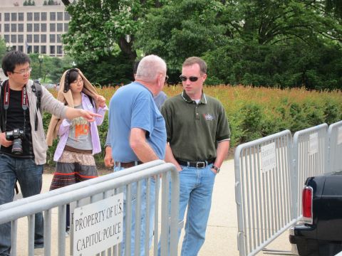 1991 Ford LTD Crown Victoria - small group of people converse beside metal barricades marked Property of US Capitol Police, near greenery.