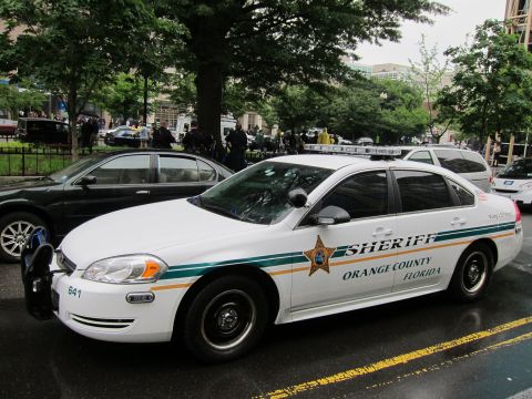 1991 Ford LTD Crown Victoria - white Orange County Florida Sheriff sedan with green and gold striping parked on a wet street near other cars.