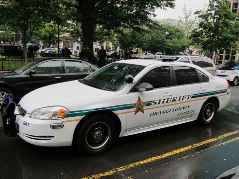 1991 Ford LTD Crown Victoria - white Orange County Florida Sheriff sedan with a gold star emblem and green striping parked on a wet street.