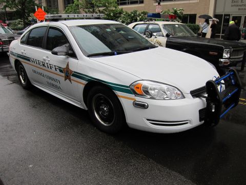 1991 Ford LTD Crown Victoria - white Orange County Florida Sheriff sedan with green striping and a front push bar parked on a wet city street.
