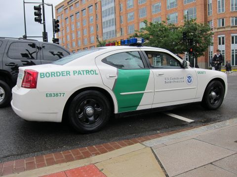 1991 Ford LTD Crown Victoria - white-and-green US Customs and Border Protection sedan with roof lights parked curbside, side profile view.