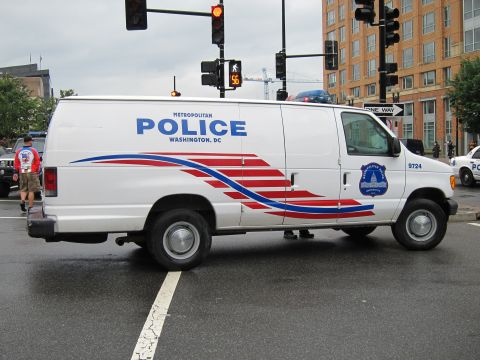 1991 Ford LTD Crown Victoria - white Metropolitan Police Washington DC cargo van marked 9724 sits at a wet downtown intersection with traffic signals overhead.