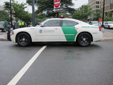 1991 Ford LTD Crown Victoria - Side profile of a white Customs and Border Protection Border Patrol sedan, E83877, parked on a rain-soaked city street.