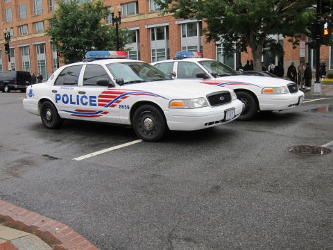 1991 Ford LTD Crown Victoria - Two white Metropolitan Police sedans with red and blue graphics, one marked 8659, parked on a wet downtown street.
