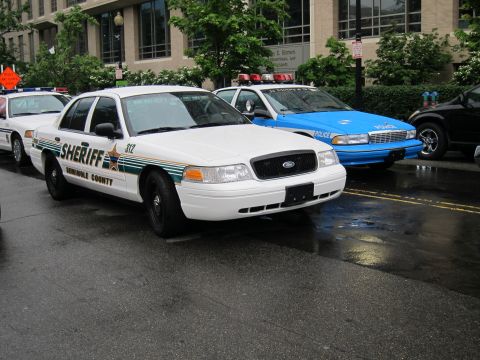 1991 Ford LTD Crown Victoria - white Seminole County Sheriff sedan marked 912 parked beside a blue police car on a rain-slicked street.