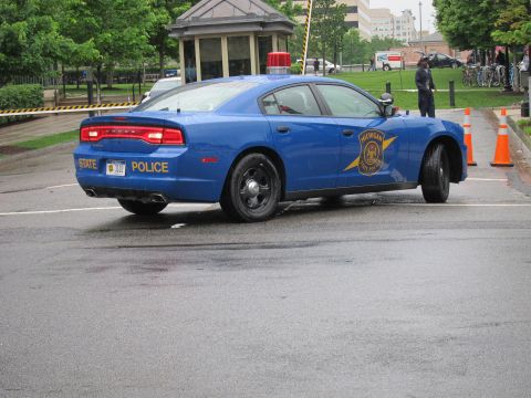 1991 Ford LTD Crown Victoria - Rear view of a blue State Police sedan on a wet road, with traffic cones and an officer standing nearby.