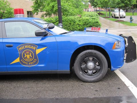 1991 Ford LTD Crown Victoria - Close side view of a blue Michigan State Police car displaying the gold star emblem and a red STOP sign mounted on the hood.