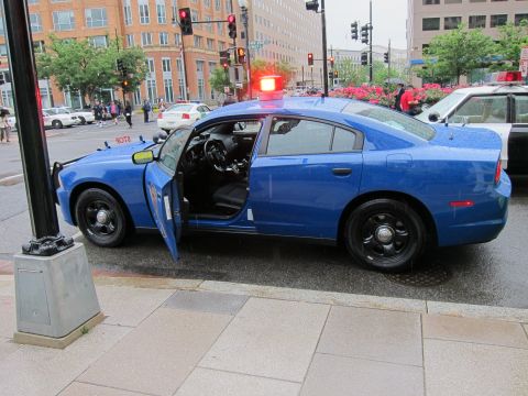 1991 Ford LTD Crown Victoria - blue Michigan State Police sedan with its driver door open, parked on a sidewalk at a rainy downtown intersection.