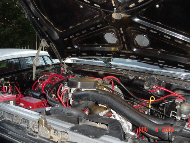 Open engine bay of a Ford truck with red plug wires, radiator hoses and battery, hood up, 2003 date