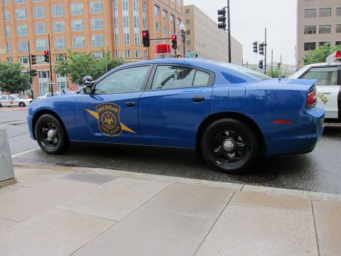 1991 Ford LTD Crown Victoria - Rear three-quarter view of a blue Michigan State Police sedan with gold star emblem parked on a wet city street.