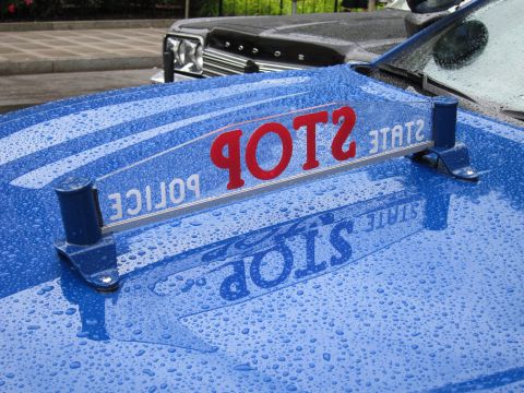 1991 Ford LTD Crown Victoria - chrome STATE POLICE STOP hood sign with red lettering, mirrored in the rain-beaded surface of a blue police car hood.