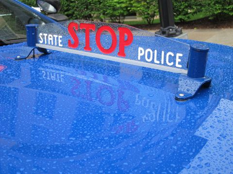 1991 Ford LTD Crown Victoria - chrome STATE POLICE hood sign with bold red STOP lettering mounted on a rain-covered blue police car hood.