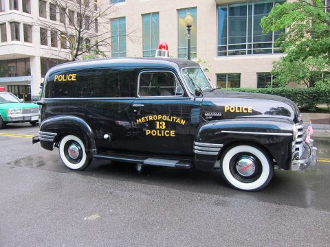 1991 Ford LTD Crown Victoria - vintage black Metropolitan Police panel van marked 13 with gold lettering and wide whitewall tires parked on a wet street.