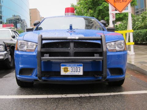 1991 Ford LTD Crown Victoria - Head-on view of a blue Dodge Charger police car with a black push bumper and Michigan plate 3103 below a red roof beacon.