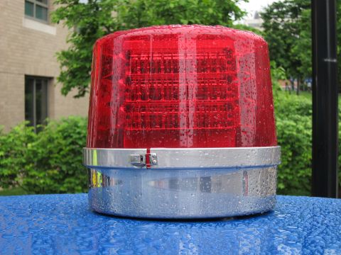 1991 Ford LTD Crown Victoria - Close-up of a round red LED rotating warning beacon with a chrome base resting on a blue tarp, beaded with water.
