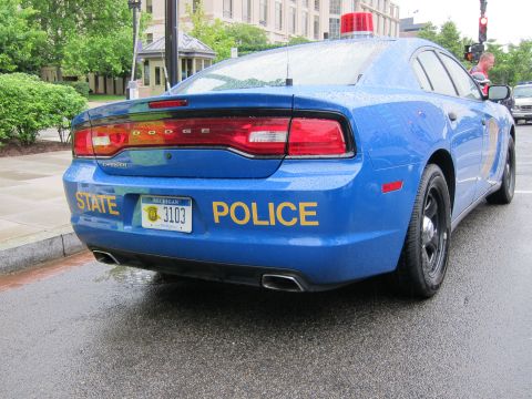 1991 Ford LTD Crown Victoria - Rear three-quarter of a blue Dodge Charger marked STATE POLICE in yellow with Michigan plate 3103 and a red roof beacon.