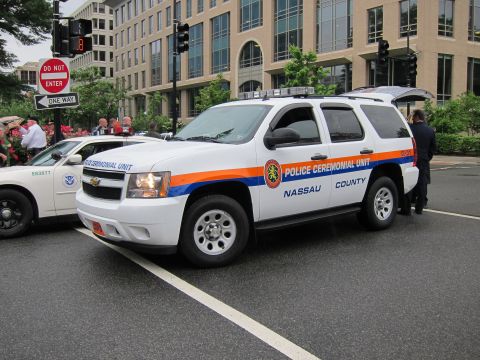 1991 Ford LTD Crown Victoria - White Chevrolet Tahoe SUV marked Police Ceremonial Unit Nassau County with orange and blue striping, parked at an intersection.