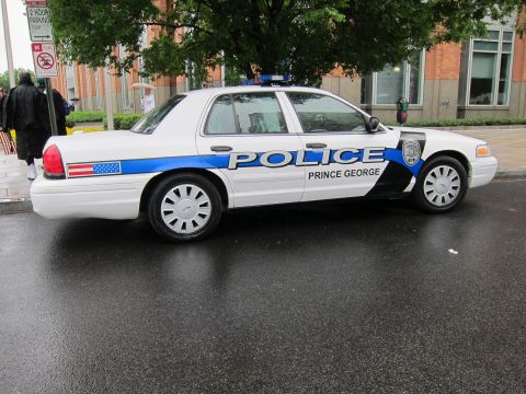 1991 Ford LTD Crown Victoria - White Ford Crown Victoria police car marked POLICE and Prince George with a blue stripe, parked on a wet street.