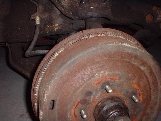 Close-up of a rusty brake drum with brake line and suspension parts visible