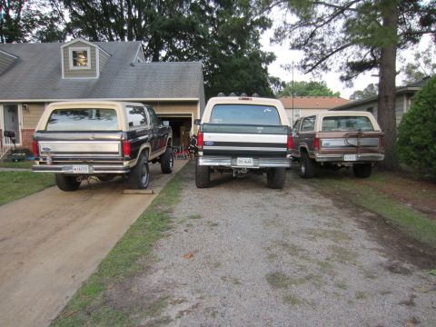 1992 Ford Bronco - Three Ford Broncos are parked in a driveway, two dark colored and one brown, all viewed from the rear.