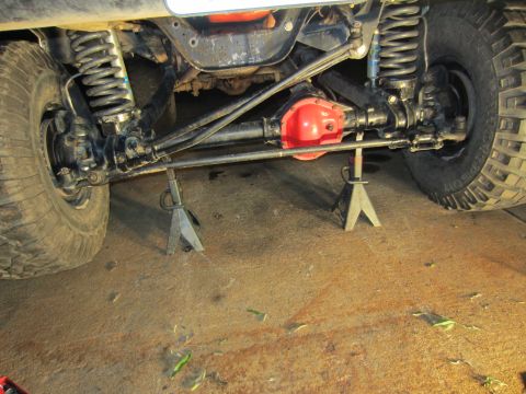 1992 Ford Bronco - The underside of a vehicle, showing the front axle, suspension, and steering linkage, is supported by jack stands.