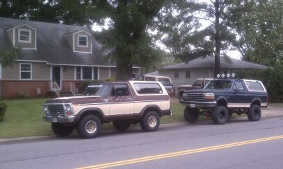 1992 Ford Bronco - Two Ford Broncos are parked on a street in front of houses, one is lifted with roof lights.