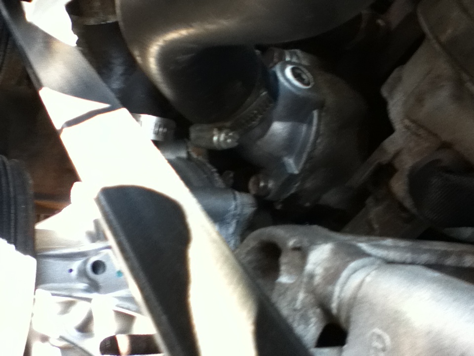 Close-up of a vehicle's engine water pump housing with hoses and a belt visible