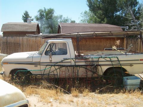 1965 Ford 427 - This 1970s pickup truck features a unique bed rack, parked in a yard with wooden fences and sheds in the background.