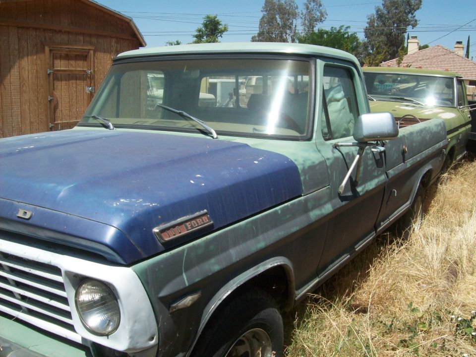 Blue and green Ford F-Series truck, front quarter view, weathered paint, chrome trim, parked next to another truck