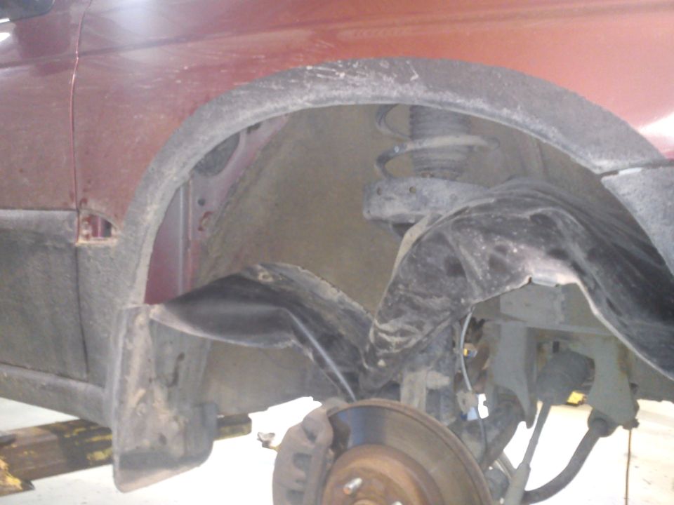 red car's front wheel well, showing suspension and brake rotor. Some rust visible