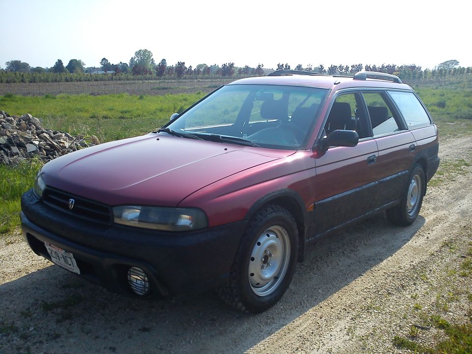 Maroon Subaru Legacy Outback wagon on steel wheels parked on a gravel farm lane