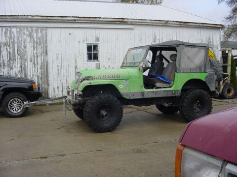 1992 Ford Bronco - A green Jeep CJ-7 Laredo is parked next to a black SUV, with a forklift visible in the background.