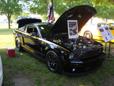 2007 Ford Mustang - A black Ford Mustang with yellow stripes is displayed with its hood open at an outdoor event.
