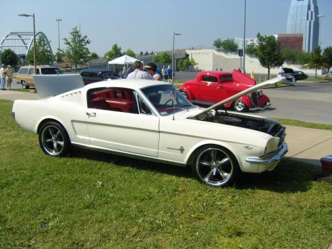 2007 Ford Mustang - A white 1965 Ford Mustang is parked on grass with its hood open, next to a red hot rod.
